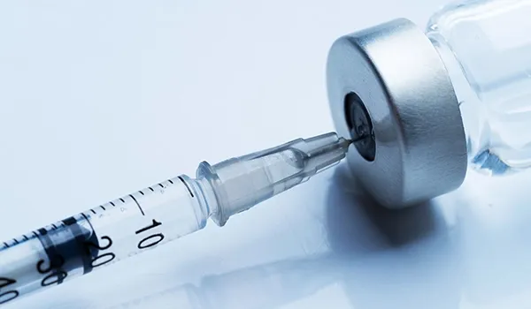 A close-up of a medical syringe with a needle inserted into a small vial, likely a therapeutic agent