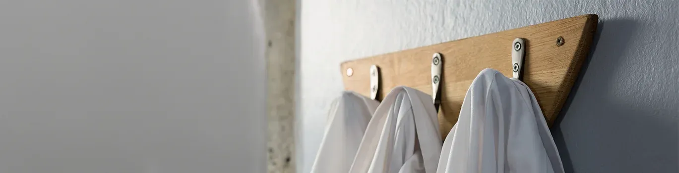 A row of white lab coats hanging on hooks against a wall.