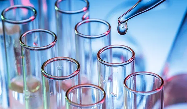 A close-up of test tubes in a laboratory setting with a pipette dispensing a liquid into one of them